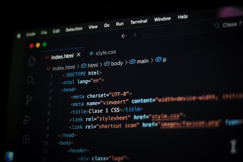 A person using a laptop with a black screen displaying lines of colorful code, situated on a dark surface in a well-lit interior space. The individual's hands are on the keyboard, and the screen shows